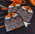 Three embroidered rectangular patches featuring gray haunted houses with orange windows, white clouds, and orange moon circles with black silhouettes, arranged on a dark patterned fabric background.