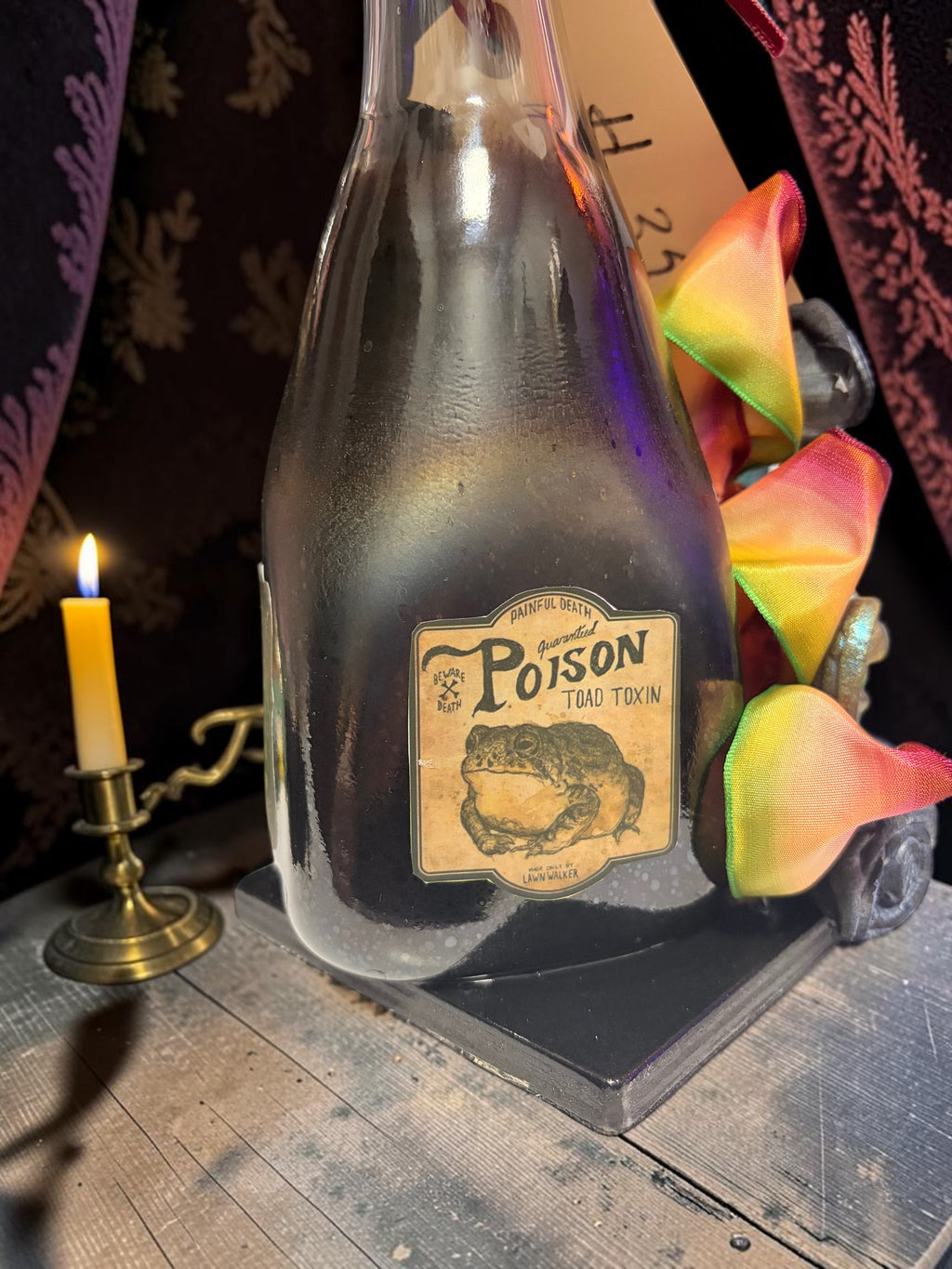 Halloween-Emporium Couture Poison bottle lamp with a vintage toad toxin label and decorative rainbow ribbon trim.