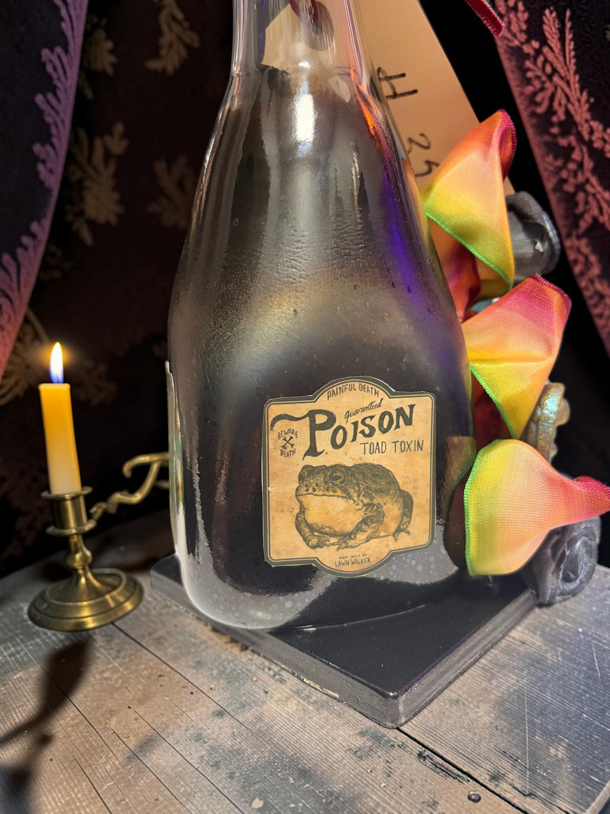 Halloween-Emporium Couture Poison bottle lamp with a vintage toad toxin label and decorative rainbow ribbon trim.