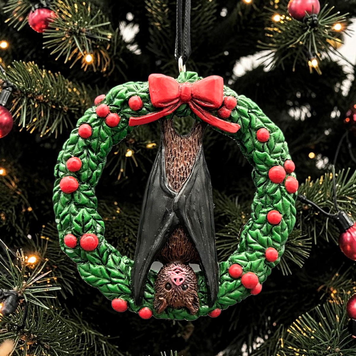 Halloween-Emporium bat ornament featuring a brown bat hanging inside a green holiday wreath with red berries and a bow.