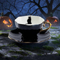 Halloween-Emporium black porcelain tea cup and saucer with gold trim and a black cat silhouette on a rustic table.