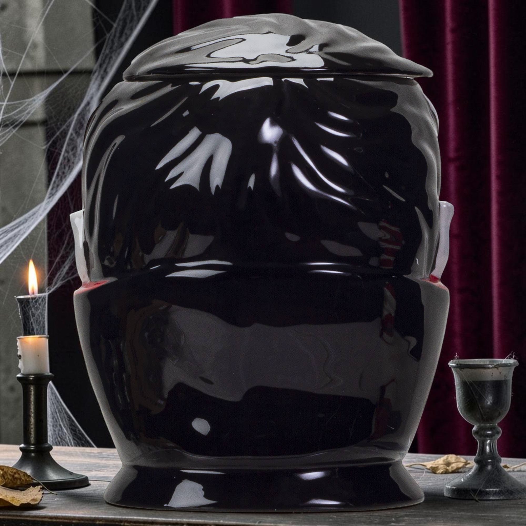 Halloween-Emporium glossy black ceramic vampire treat jar with a removable lid, displayed on a rustic table.