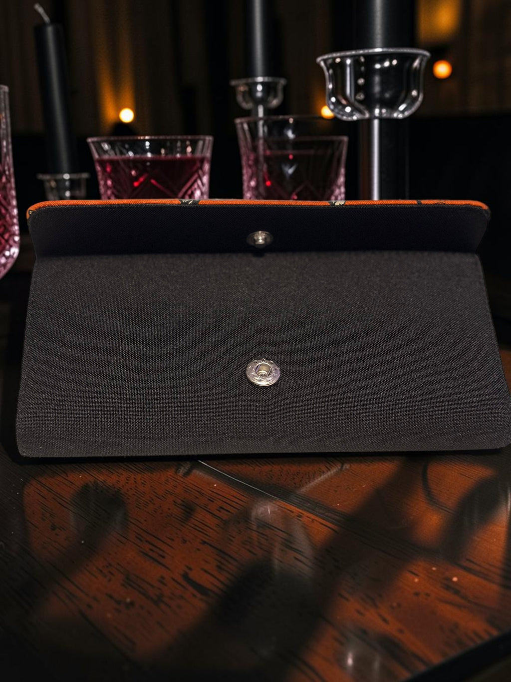 Halloween-Emporium black clutch wallet with a snap button closure, displayed on a dark wooden table.