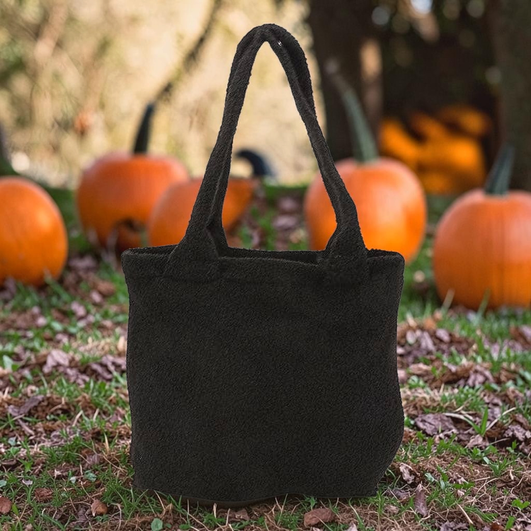 Halloween-Emporium black furry cat tote bag with a soft plush texture, displayed outdoors among autumn pumpkins.