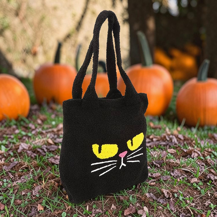 Halloween-Emporium black furry tote bag with a grumpy yellow-eyed cat face design, set against a pumpkin patch.
