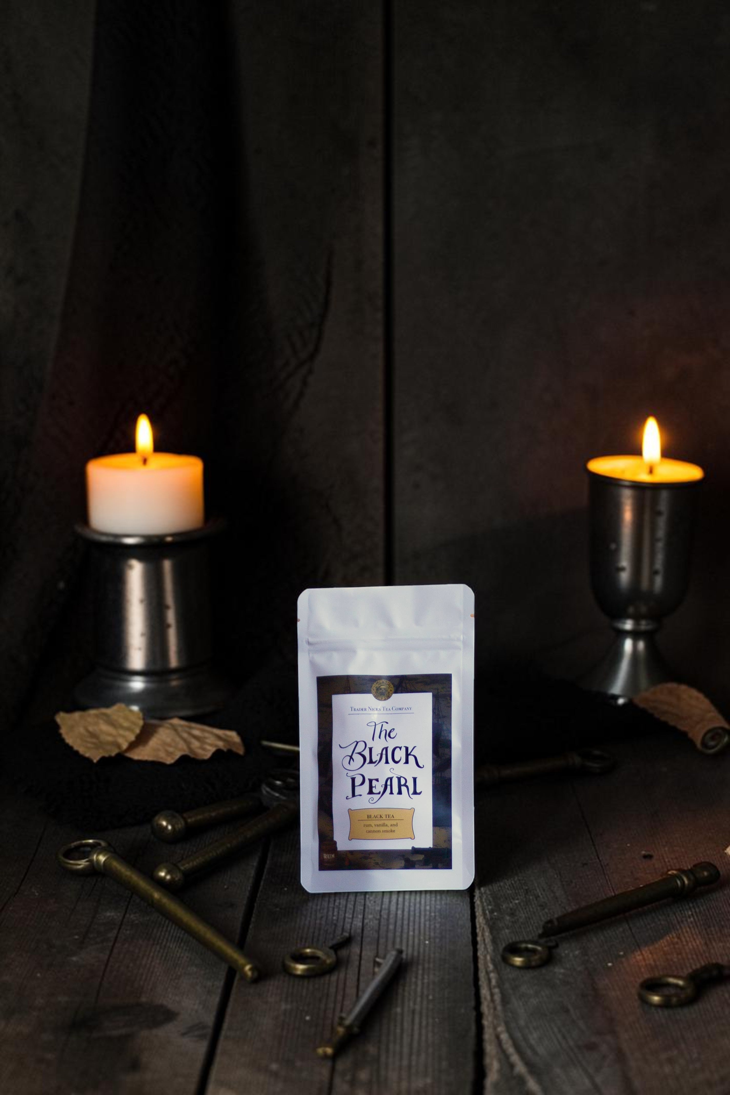 Halloween-Emporium The Black Pearl smoked black tea pouch displayed on a dark wooden table with candles and antique keys.