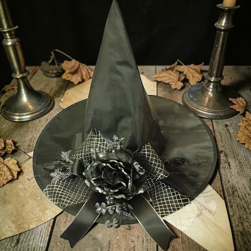 Halloween-Emporium black witch hat featuring a decorative black rose, ribbon, and netting on a rustic wooden table.