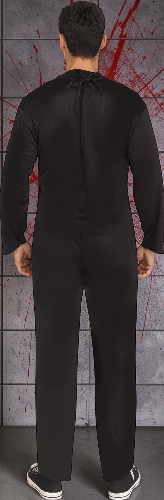 Halloween-Emporium adult black skeleton jumpsuit shown from the back against a grey tiled wall with red blood splatter