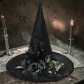 Halloween-Emporium black witch hat featuring a skull and dark gothic flowers on a table with lit candles.