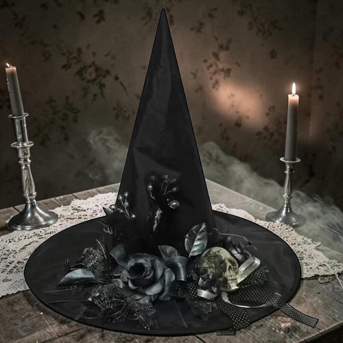 Halloween-Emporium black witch hat featuring a skull and dark gothic flowers on a table with lit candles.