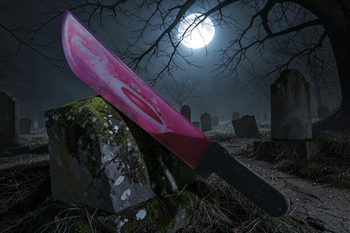 Halloween-Emporium 24-inch bleeding machete prop with realistic blood effect resting on a mossy tombstone at night.
