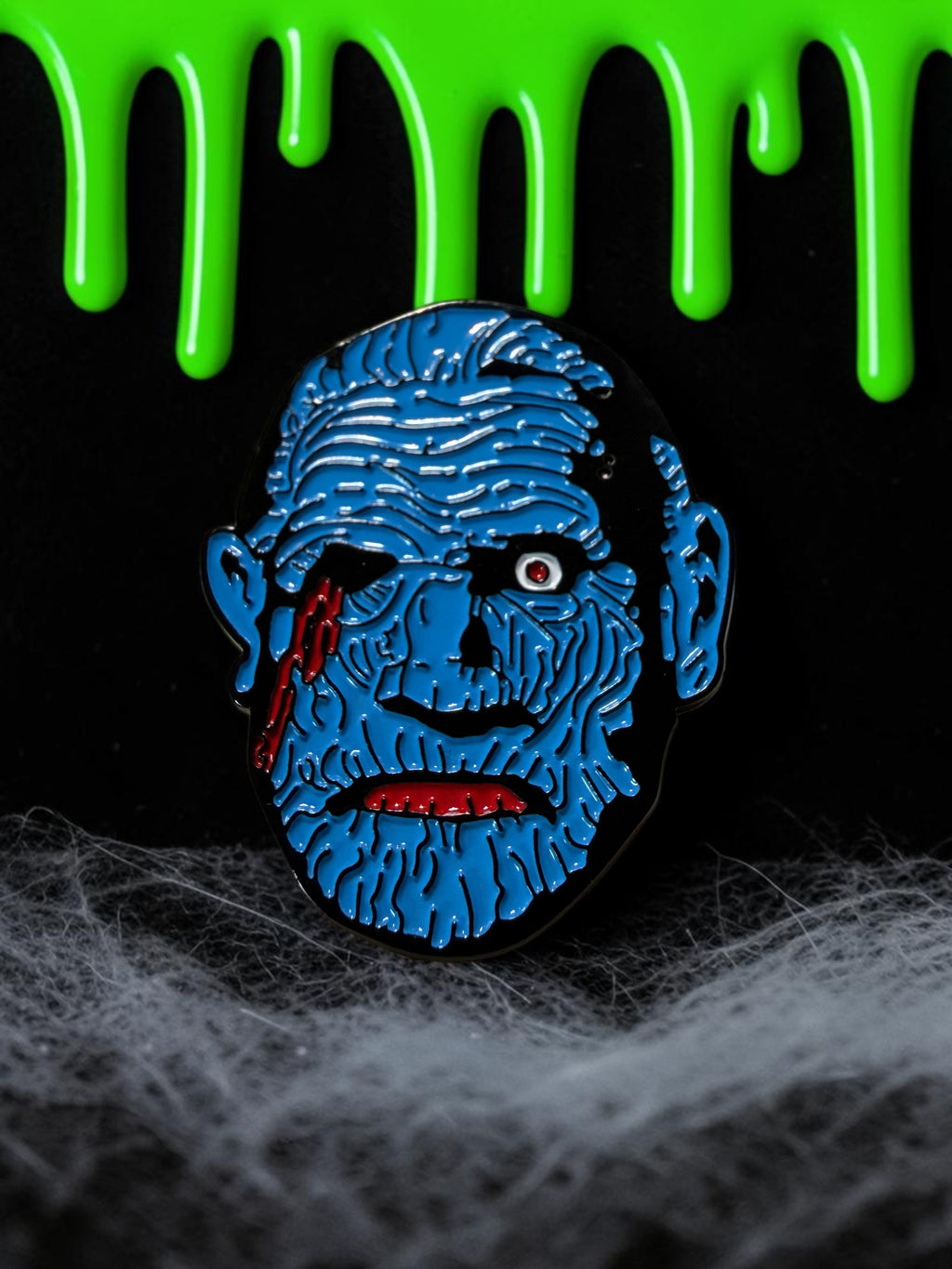 Halloween-Emporium 1.5-inch blue zombie enamel pin with red blood details on a spooky black background