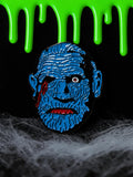 Halloween-Emporium 1.5-inch blue zombie enamel pin with red blood details on a spooky black background