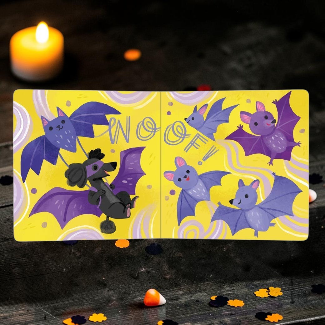 Halloween-Emporium Boo Bark! board book open to a page with a black poodle in a bat costume flying with purple bats.