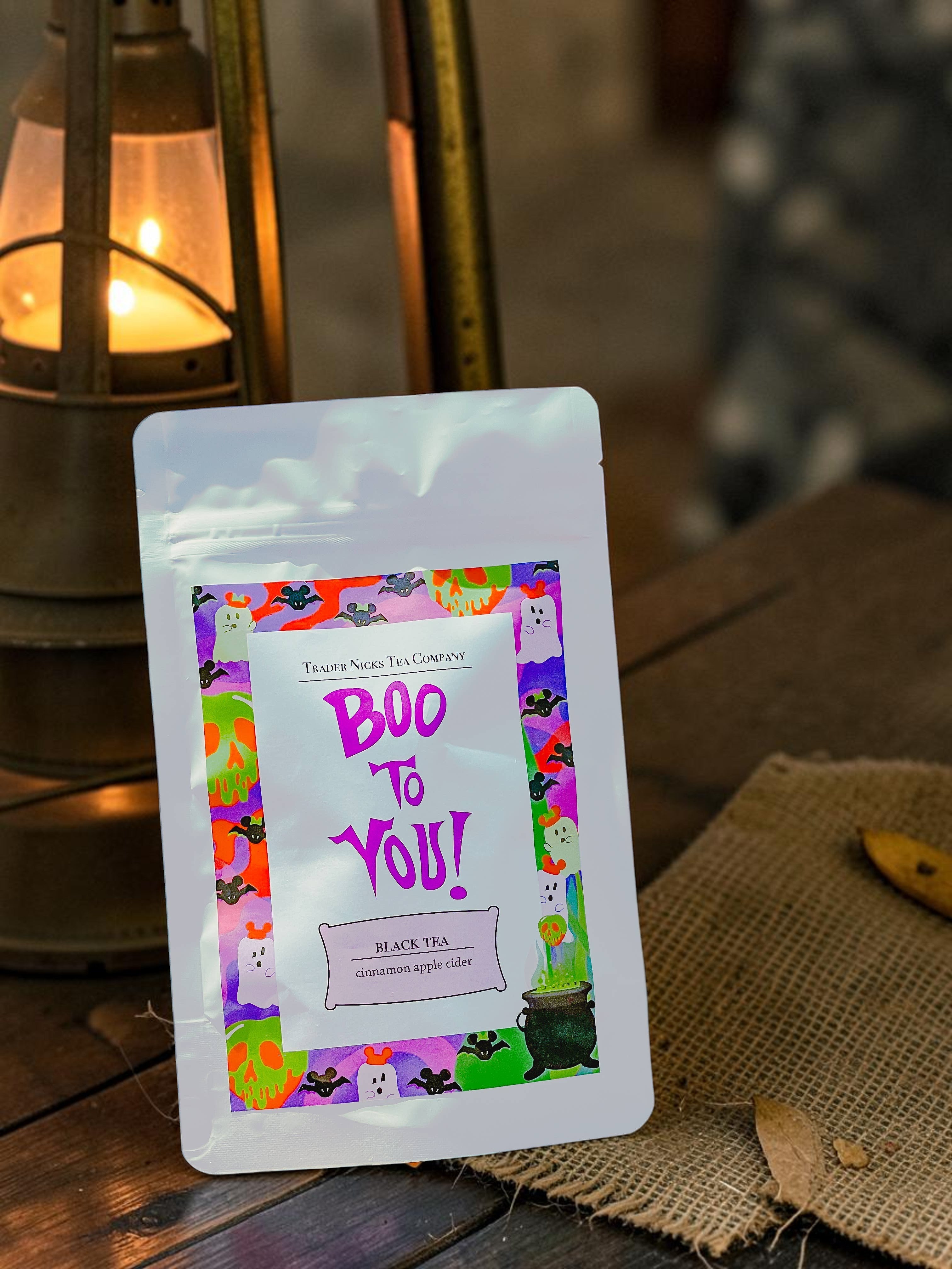 Halloween-Emporium Boo to You black tea pouch with festive ghost and bat label art next to a glowing lantern.