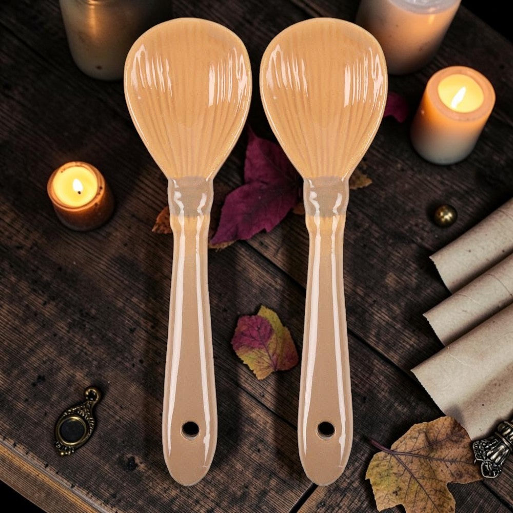 Halloween-Emporium set of two glossy tan ceramic spoons shaped like whimsical witch broomsticks on a rustic table.