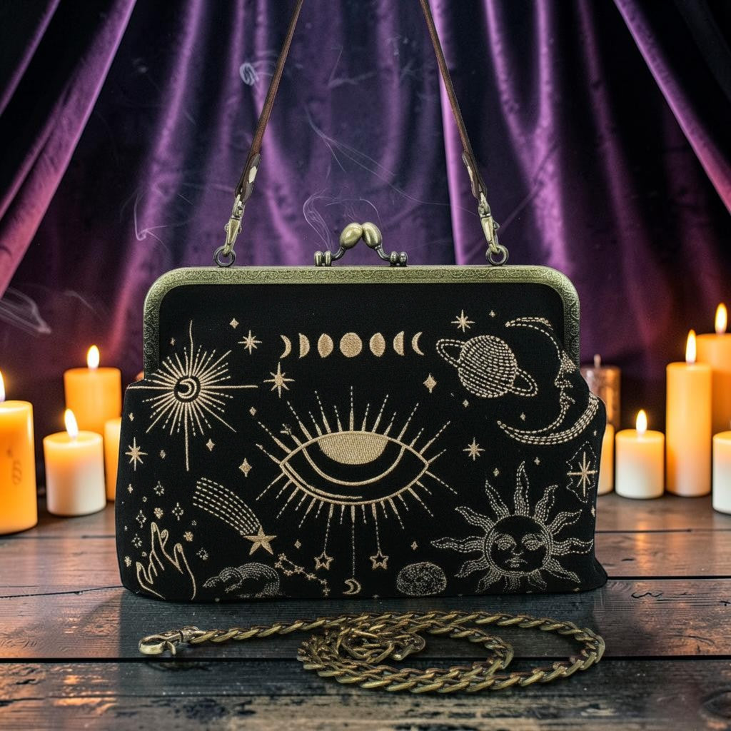 Halloween-Emporium black kisslock handbag with gold embroidered celestial moon and sun motifs on a candlelit table.