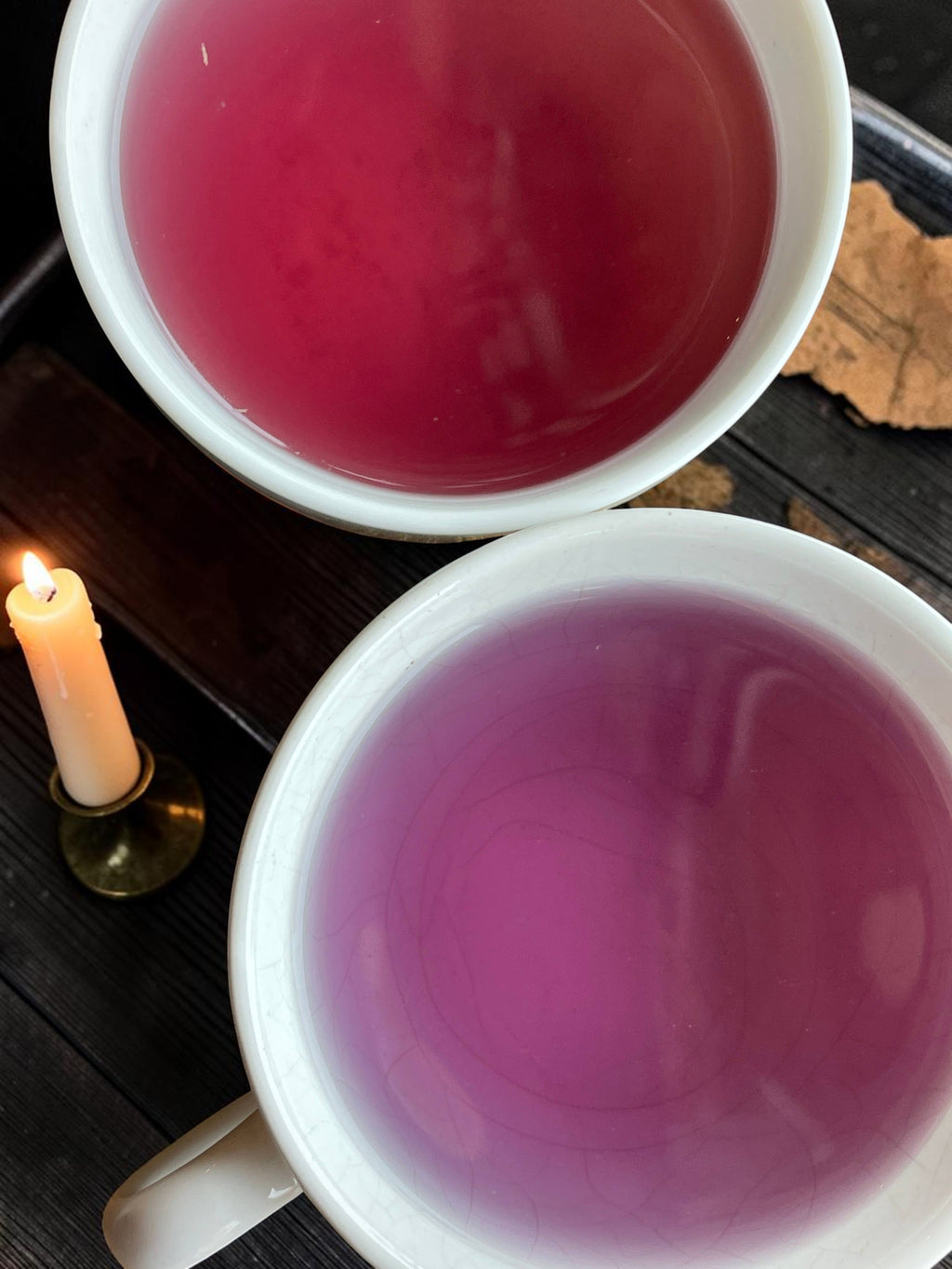 Halloween-Emporium Sea Witch cherry coconut fruit tea in two white mugs with a lit candle on a dark wooden table
