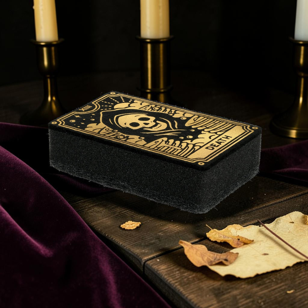 Halloween-Emporium Death tarot card kitchen sponge with metallic gold skull illustration on a dark wooden table.