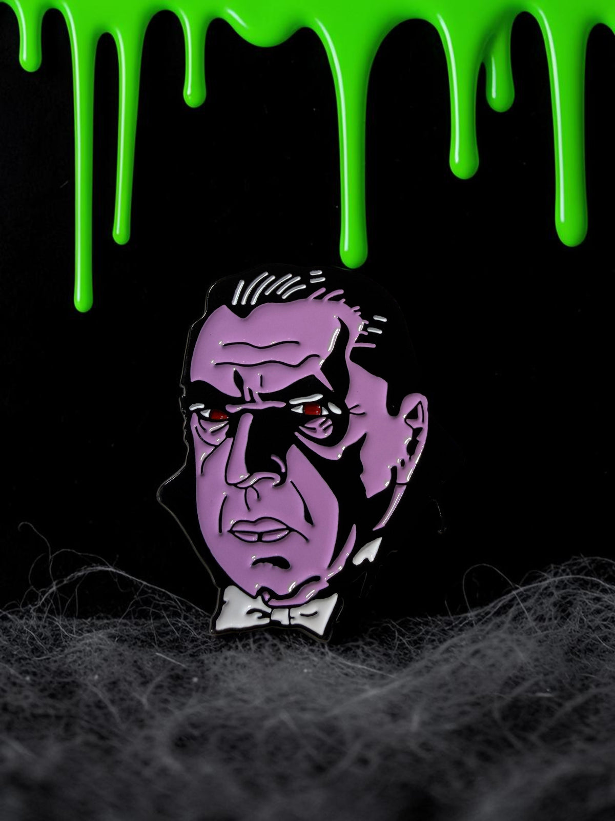 Halloween-Emporium Dracula enamel pin featuring a detailed purple vampire portrait with red eyes and a white bowtie.