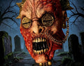 Halloween-Emporium Famine Black Horseman latex mask with decaying skin, coin eyes, and gold chain in a graveyard.