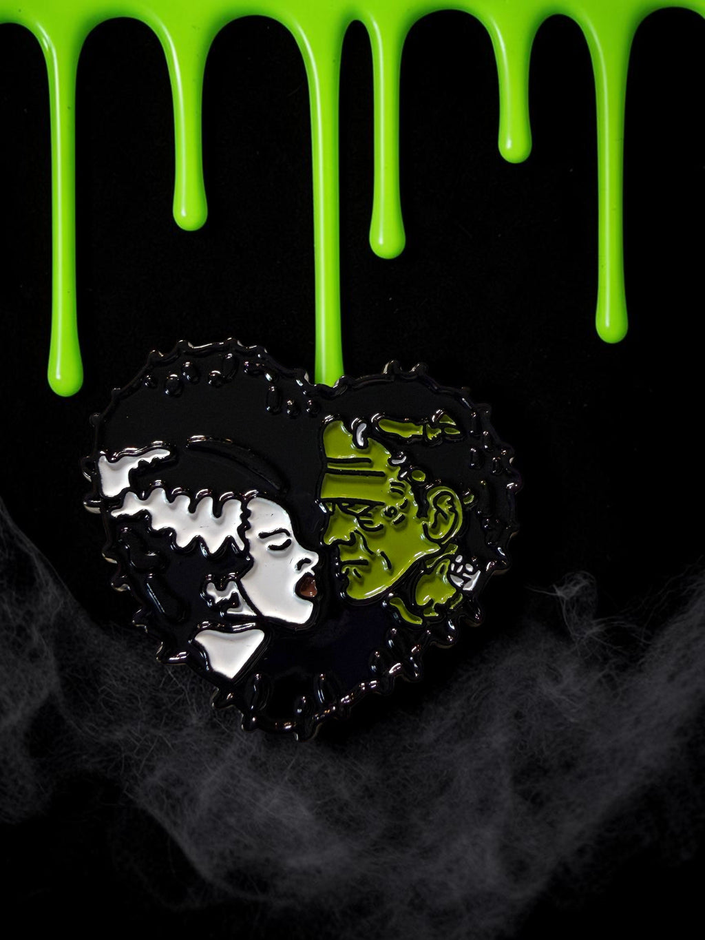 Halloween-Emporium Frankenstein and Bride heart-shaped soft enamel pin with green and black details.