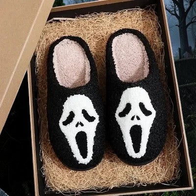 Halloween-Emporium plush black house slippers featuring a white Ghost Face mask design in a gift box with straw.