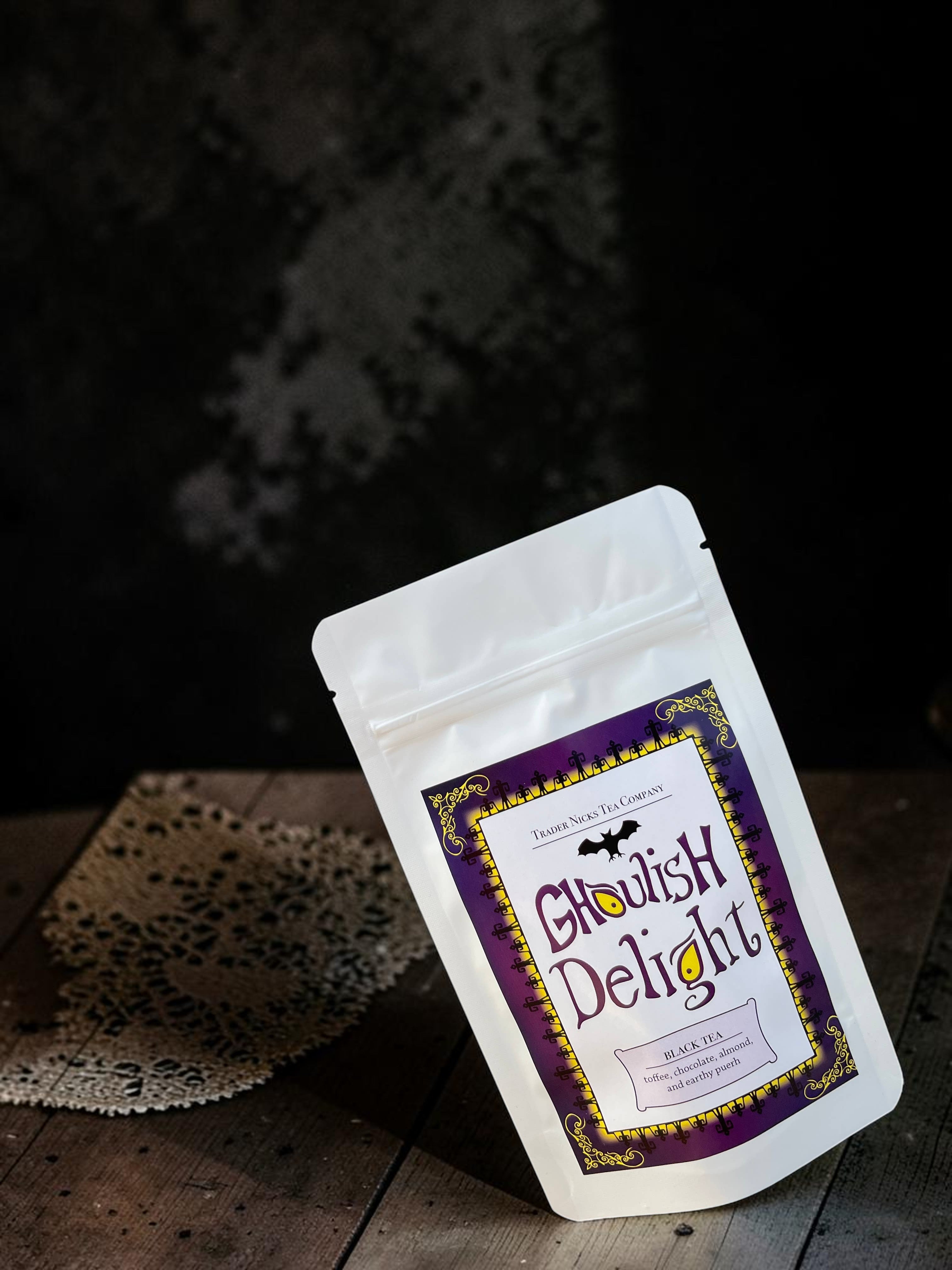 Halloween-Emporium Ghoulish Delight black tea pouch with purple label, bat graphic, and gothic border on wooden table