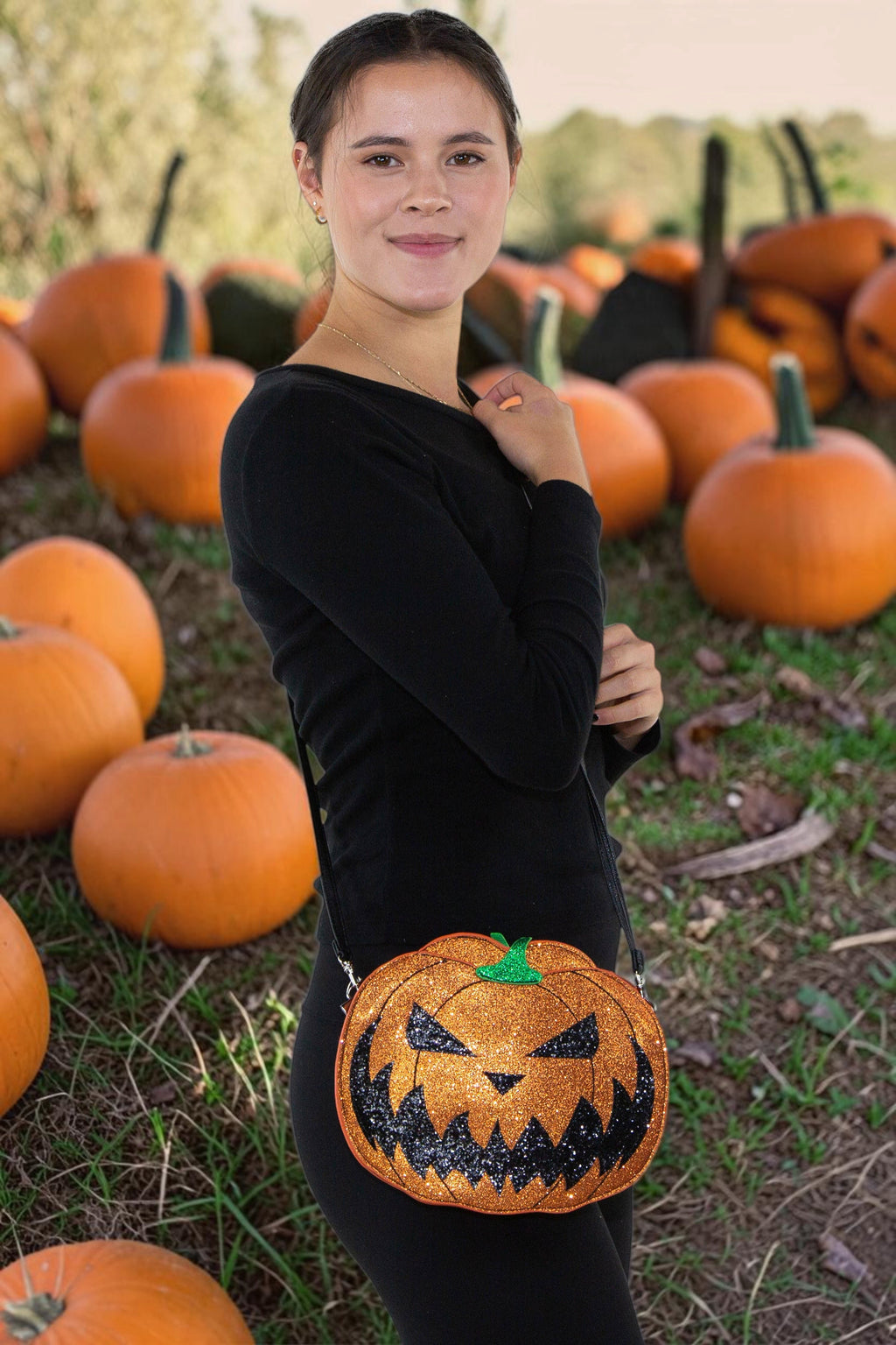 Halloween-Emporium glittery orange jack-o-lantern vinyl crossbody bag with adjustable strap in a pumpkin patch.