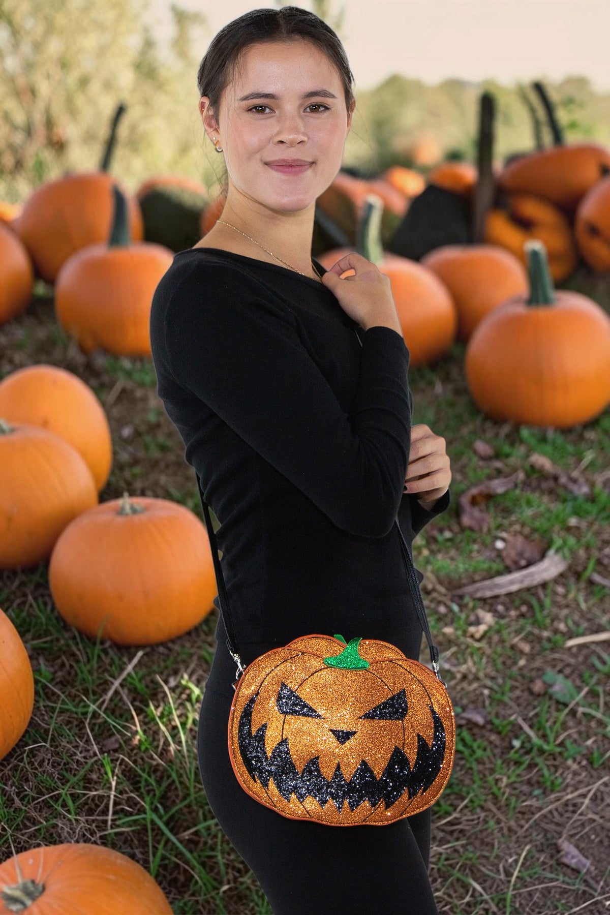 Halloween-Emporium glittery orange jack-o-lantern vinyl crossbody bag with adjustable strap in a pumpkin patch.