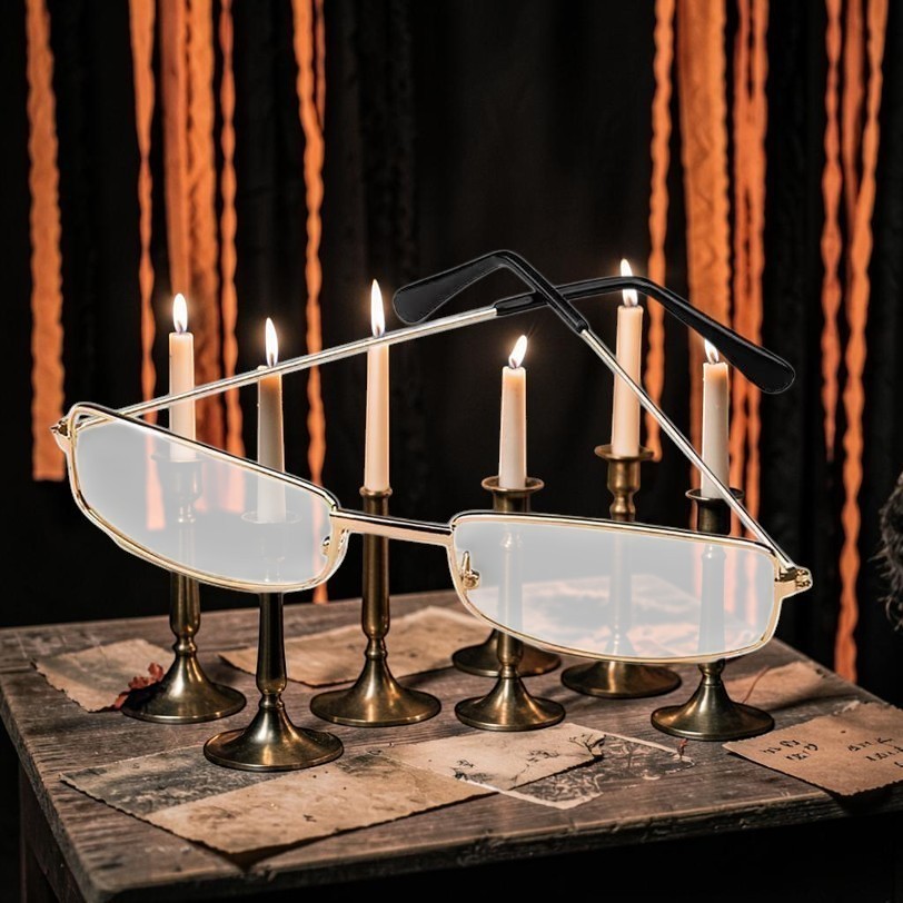 Halloween-Emporium rectangular costume glasses with gold metal frames and clear lenses on a candlelit table