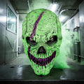 Halloween-Emporium neon green monster latex mask with purple fangs and skull details in a smoky hallway.