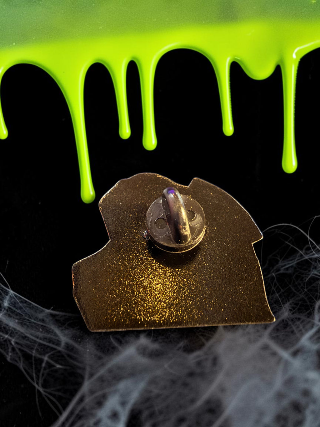 Halloween-Emporium My Name is Guirmo enamel pin back view showing metal clutch on a black surface with green slime