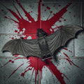 Halloween-Emporium matte black PVC hanging bat wall decoration with detailed wings against a blood-splattered wall.