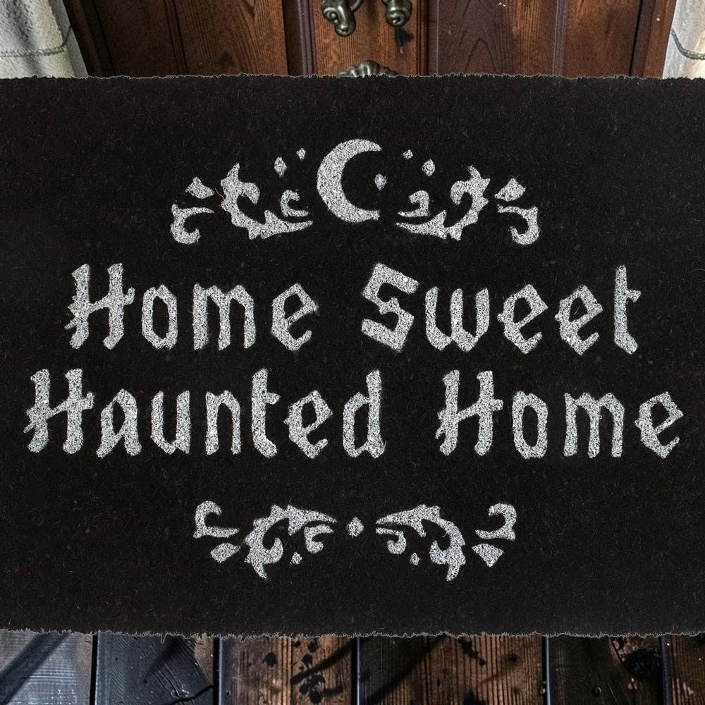Halloween-Emporium natural grass doormat with Home Sweet Haunted Home text and crescent moon design in black and silver.
