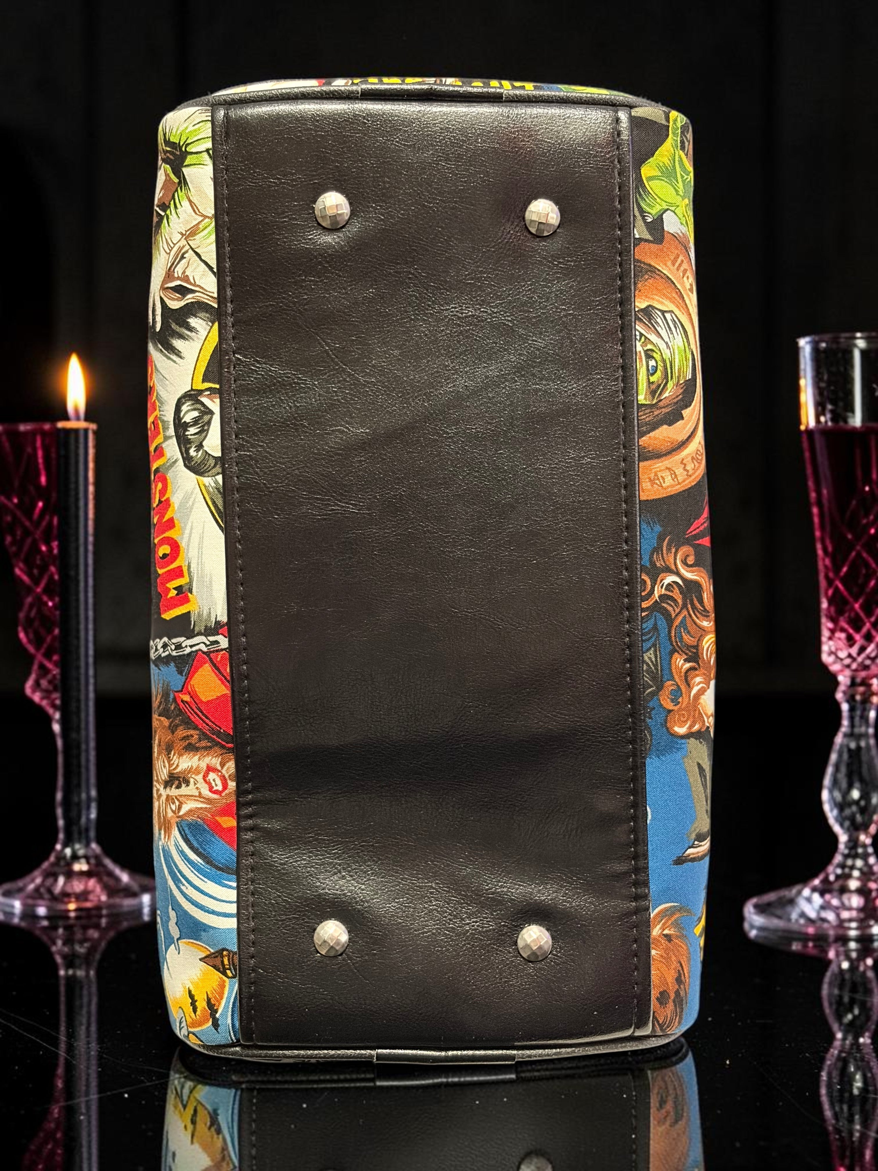 Halloween-Emporium purple classic horror handbag with a black leather base and metal feet on a dark reflective surface