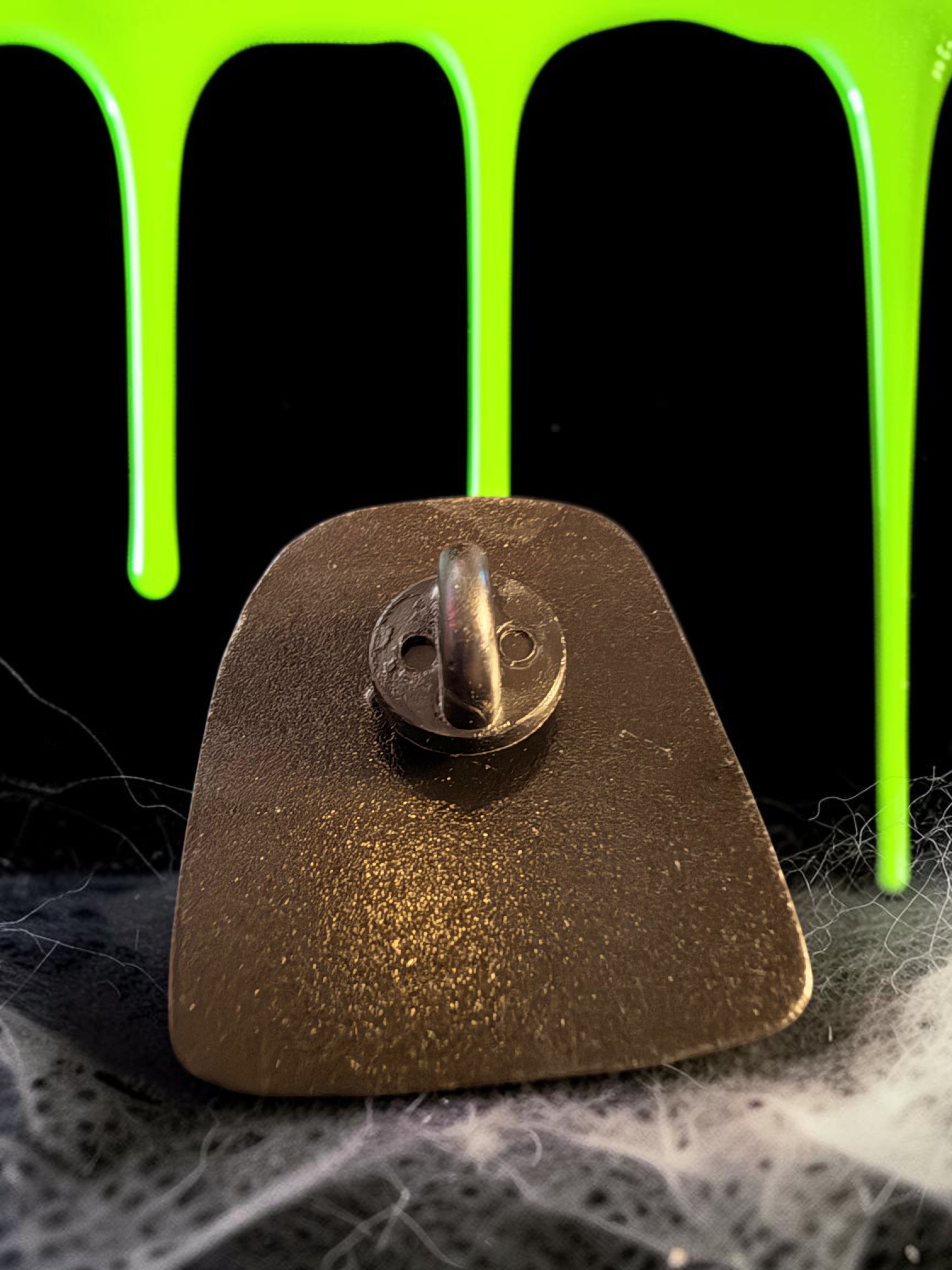Halloween-Emporium Jackie Daytona enamel pin back view showing the metal clutch against a green slime background.