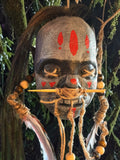 Halloween-Emporium latex shrunken head with red face paint, hand-punched hair, twine stitching, and red feathers.
