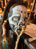 Halloween-Emporium latex voodoo shrunken head mask with tribal markings, synthetic hair, jute rope, and feather accents.