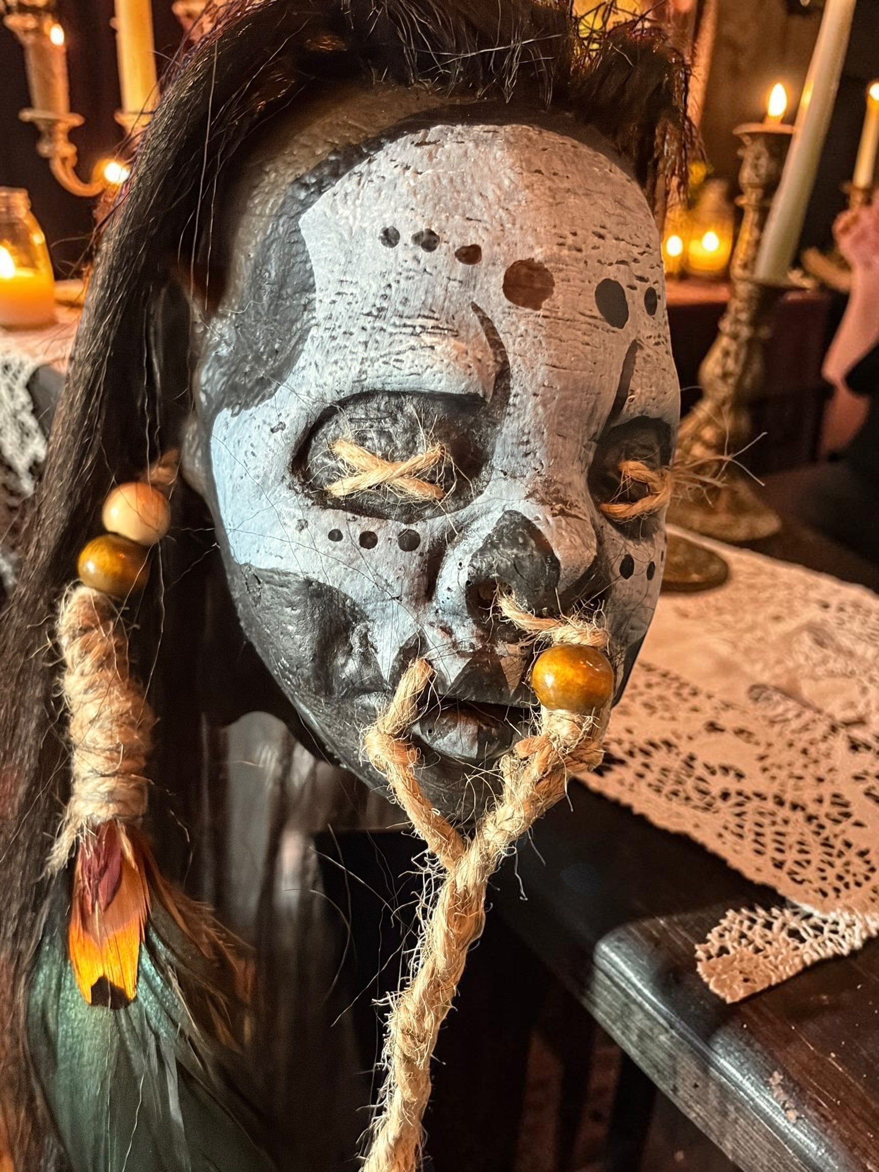 Halloween-Emporium latex voodoo shrunken head mask with tribal markings, synthetic hair, jute rope, and feather accents.