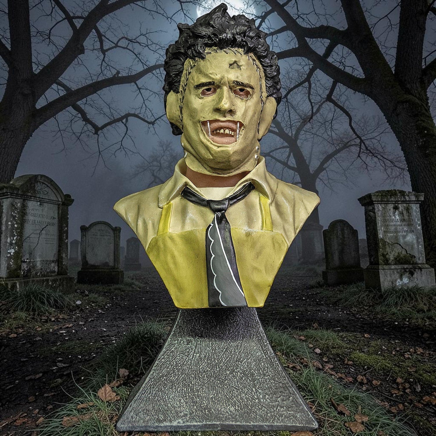 Halloween-Emporium Leatherface mini bust featuring detailed mask and yellow apron in a spooky graveyard setting.