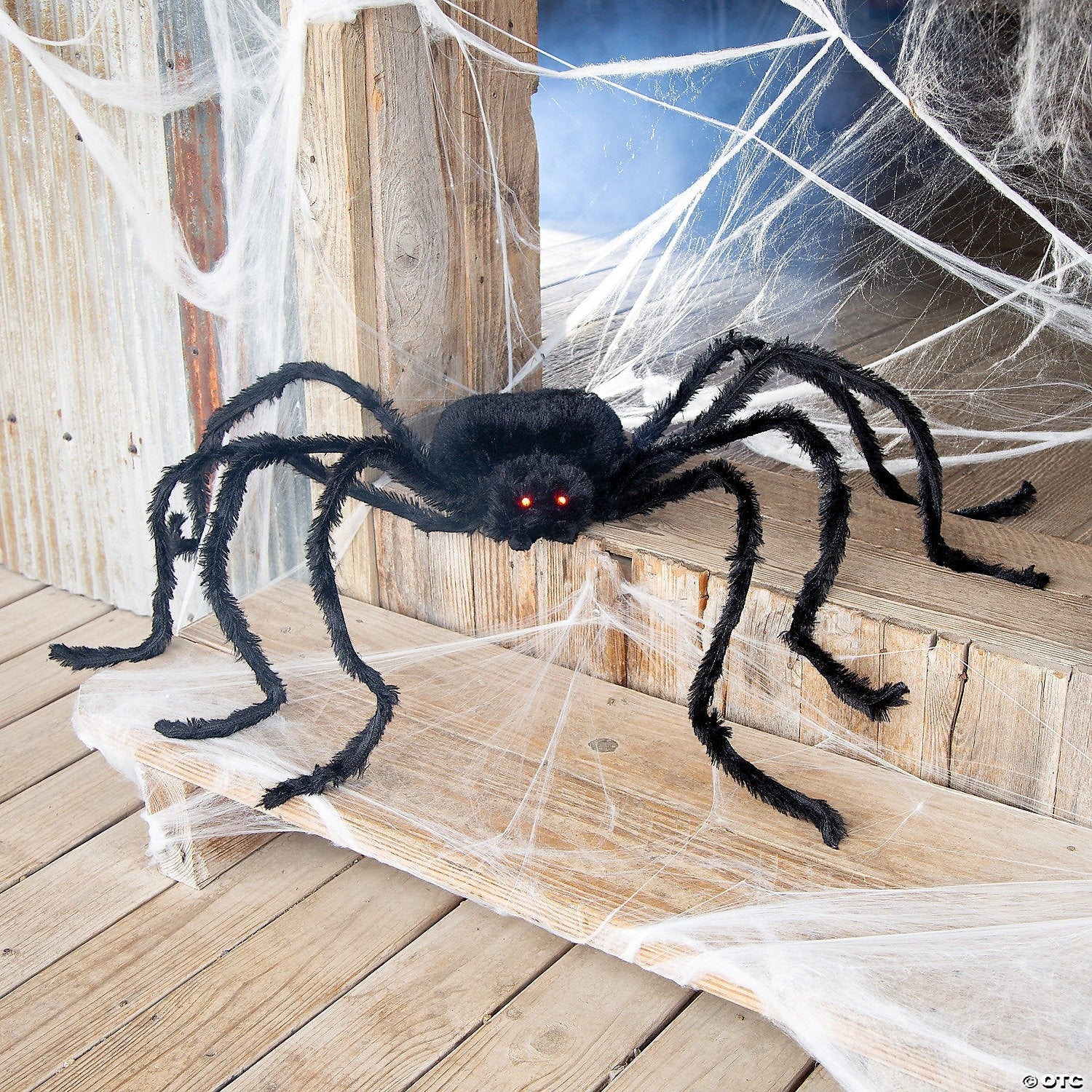 Halloween-Emporium oversized black shaggy spider prop with glowing red eyes and poseable legs on a wooden porch.