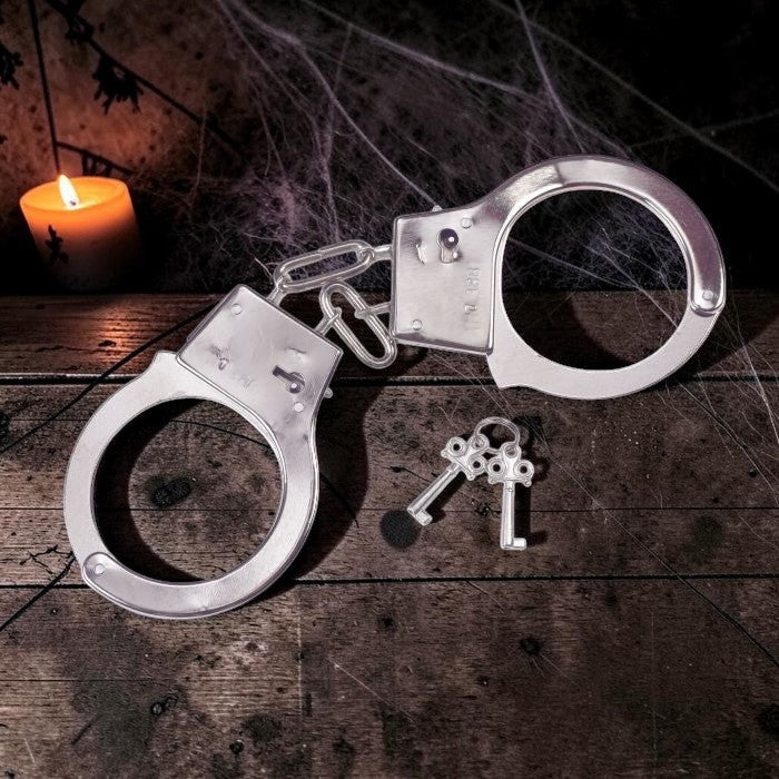 Halloween-Emporium silver metal costume handcuffs with two keys on a dark wooden table with a candle