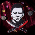 Halloween-Emporium large Michael Myers embroidered patch with crossed bloody knives on a dark red velvet background.