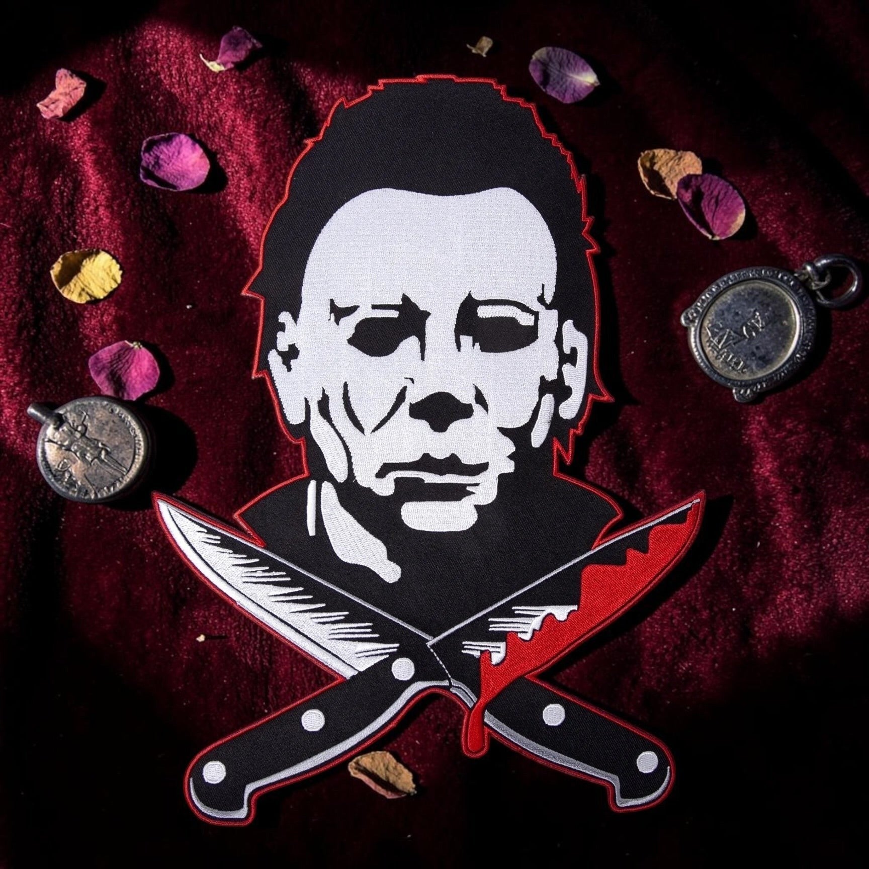Halloween-Emporium large Michael Myers embroidered patch with crossed bloody knives on a dark red velvet background.