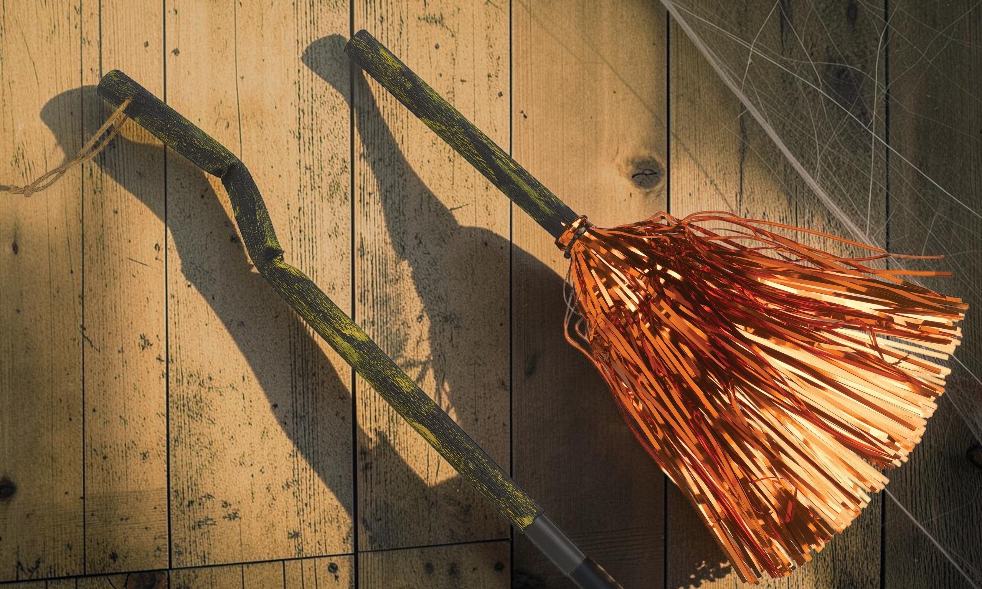 Halloween-Emporium hanging witch broomstick prop with a rustic gnarled handle and shimmering orange tinsel bristles.