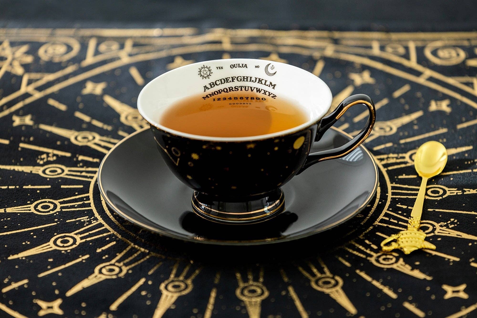 Halloween-Emporium porcelain tea cup and saucer set featuring a black exterior with gold constellations and Ouija board