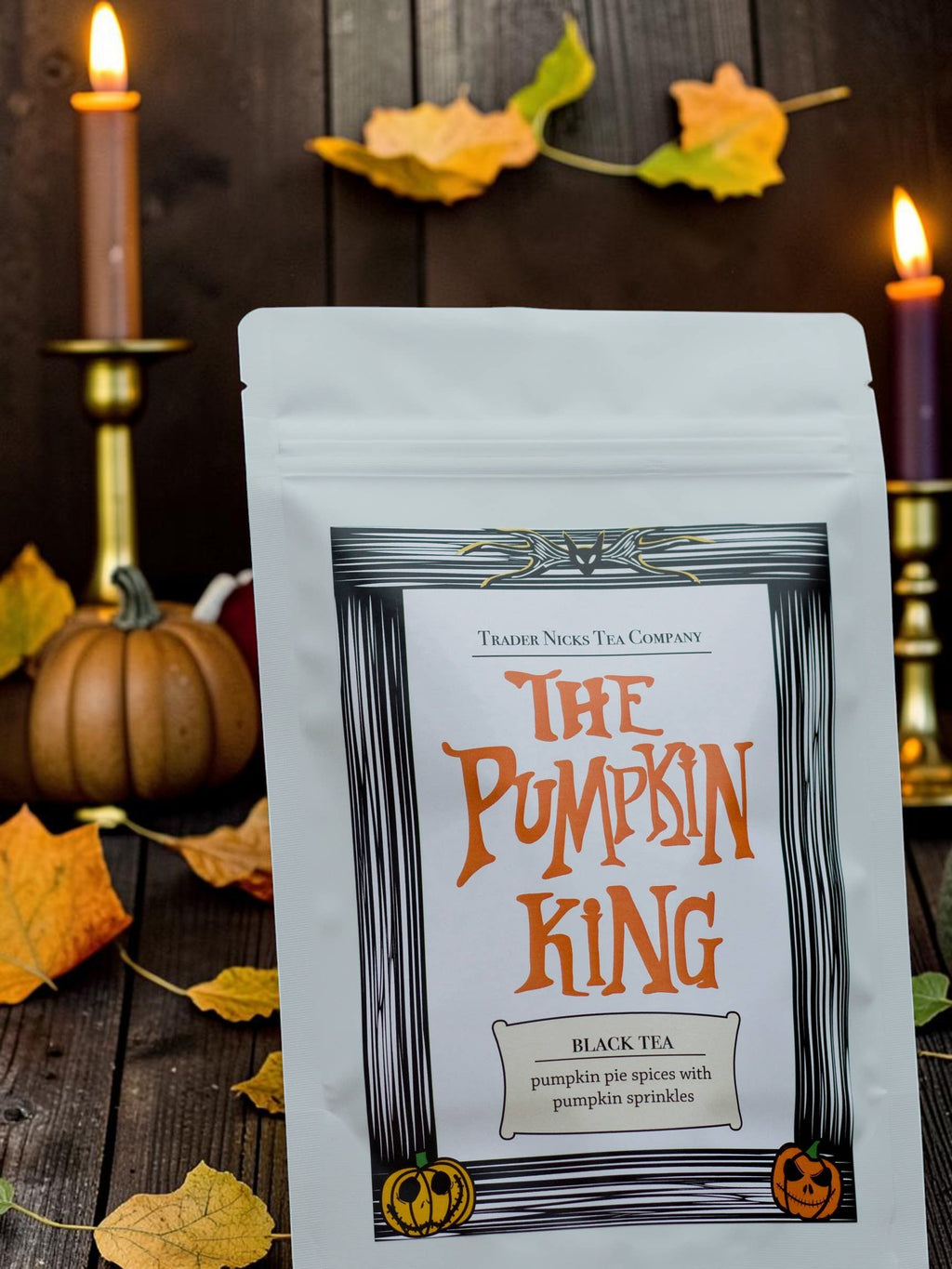 Halloween-Emporium Pumpkin King Chai black tea in a white pouch, set on a rustic table with autumn leaves and candles.