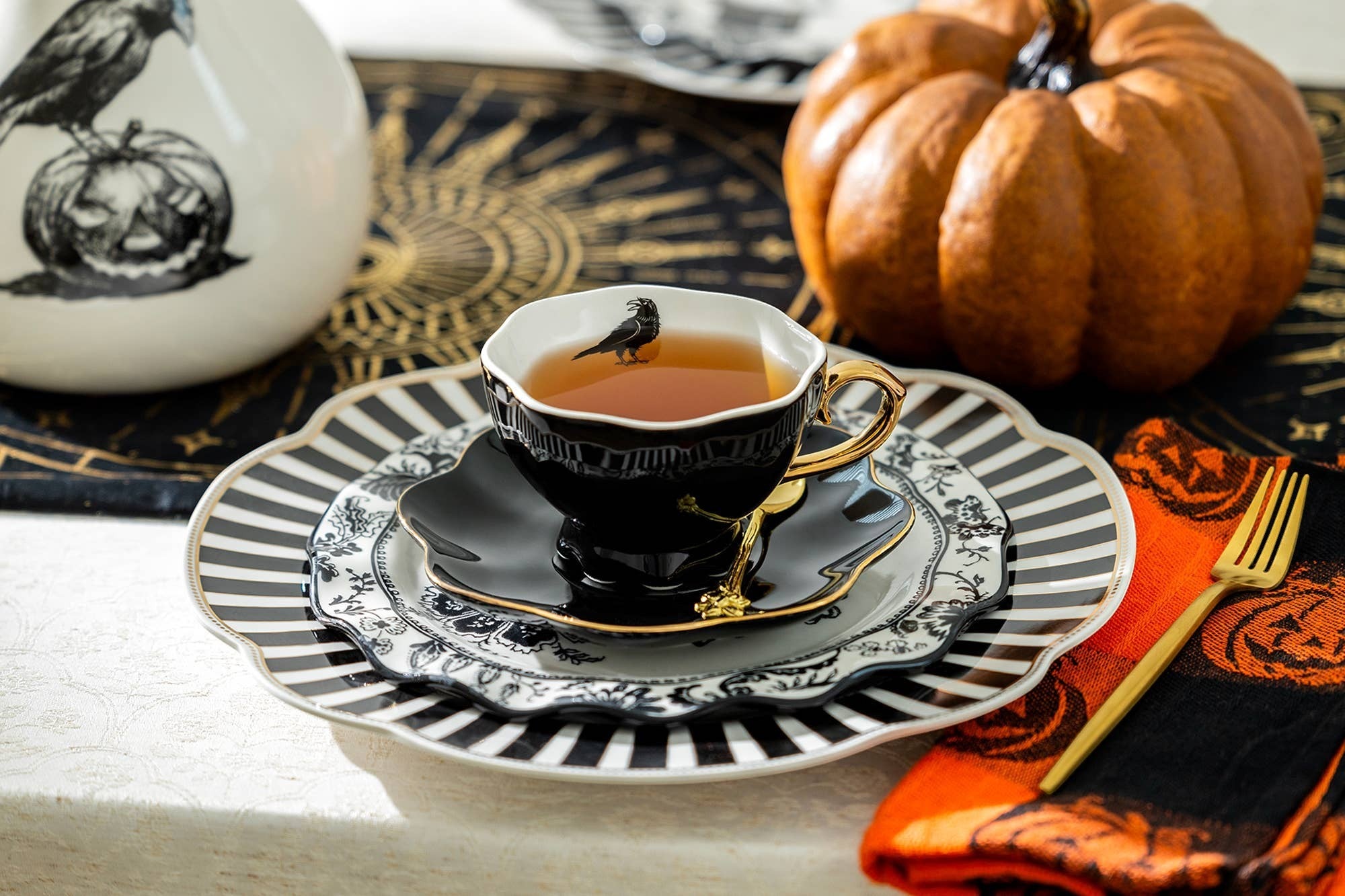 Halloween-Emporium Raven Black Gold tea cup and saucer with a raven motif, gold handle, and scalloped edges on a table.