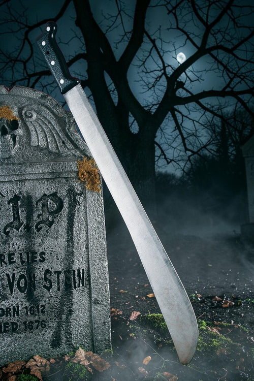 Halloween-Emporium 27-inch realistic machete costume prop with weathered metallic blade leaning on a stone tombstone.